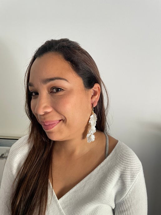 Woman wearing large, white, ruffled earrings against a neutral background