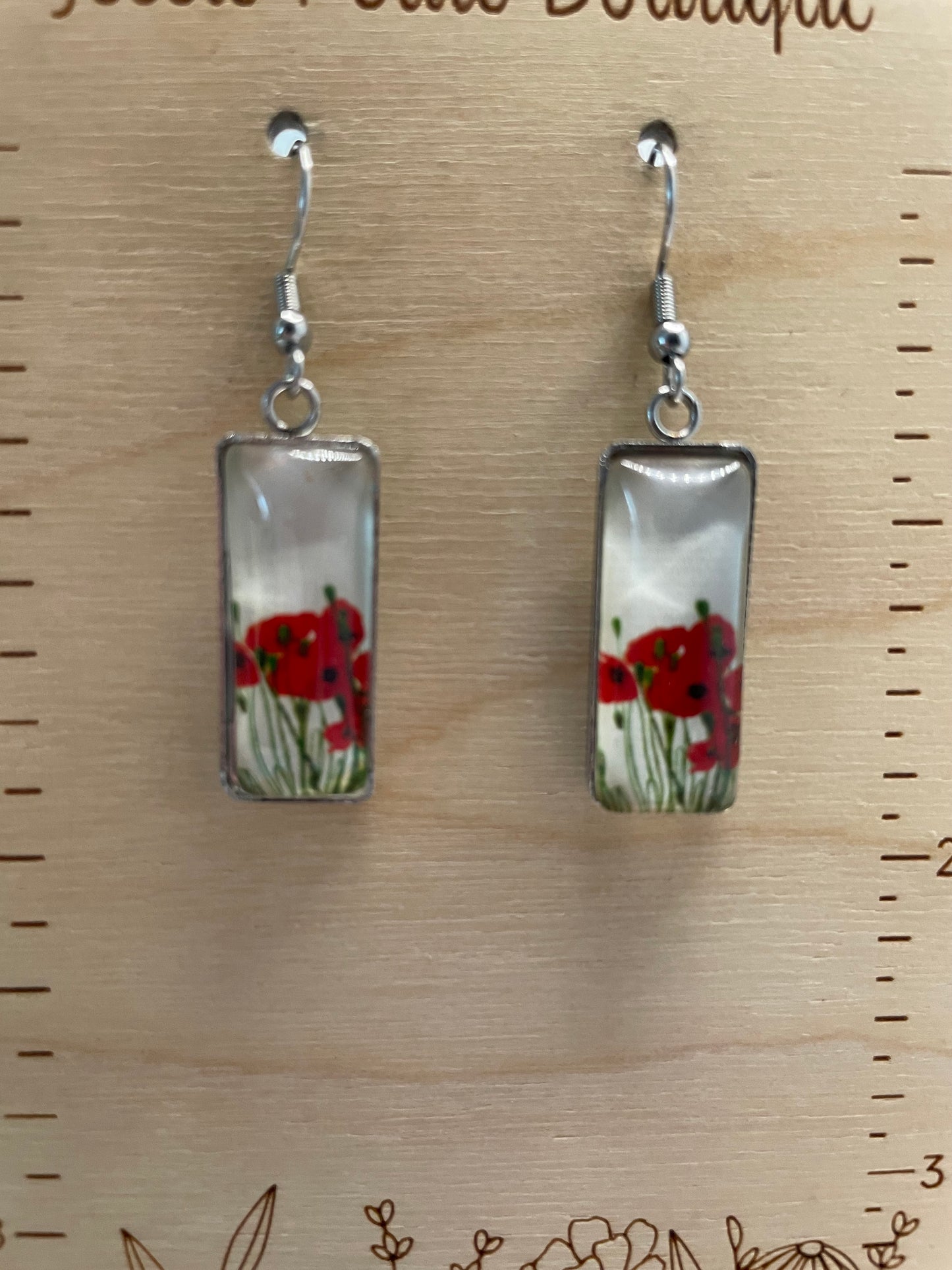 Two rectangular earrings with floral design on a wooden surface with ruler for scale.