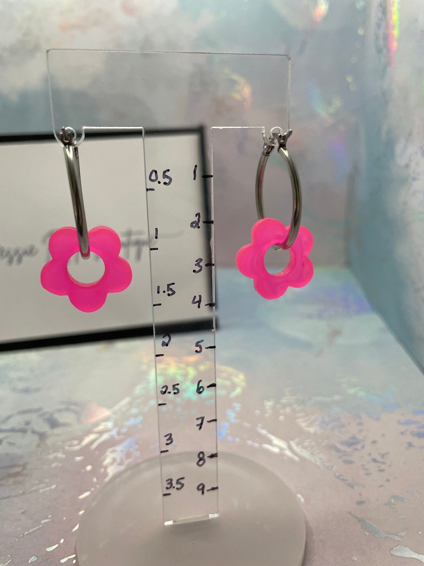 Earrings with pink flower charms on a transparent ruler for size reference.