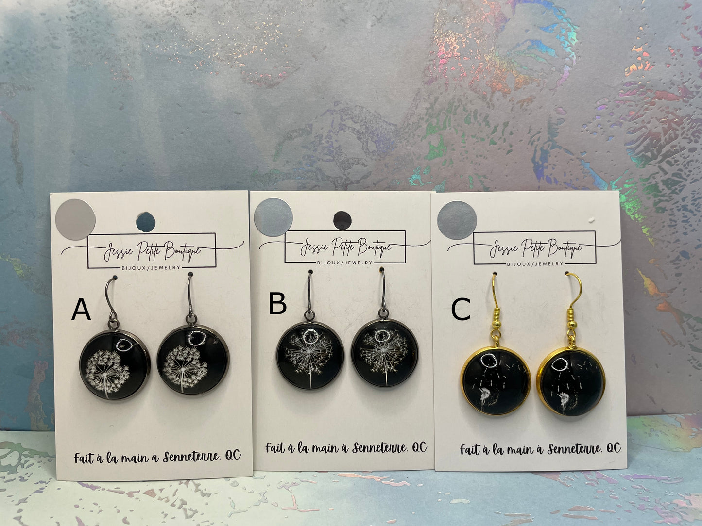 Three pairs of earrings on display cards with a decorative background