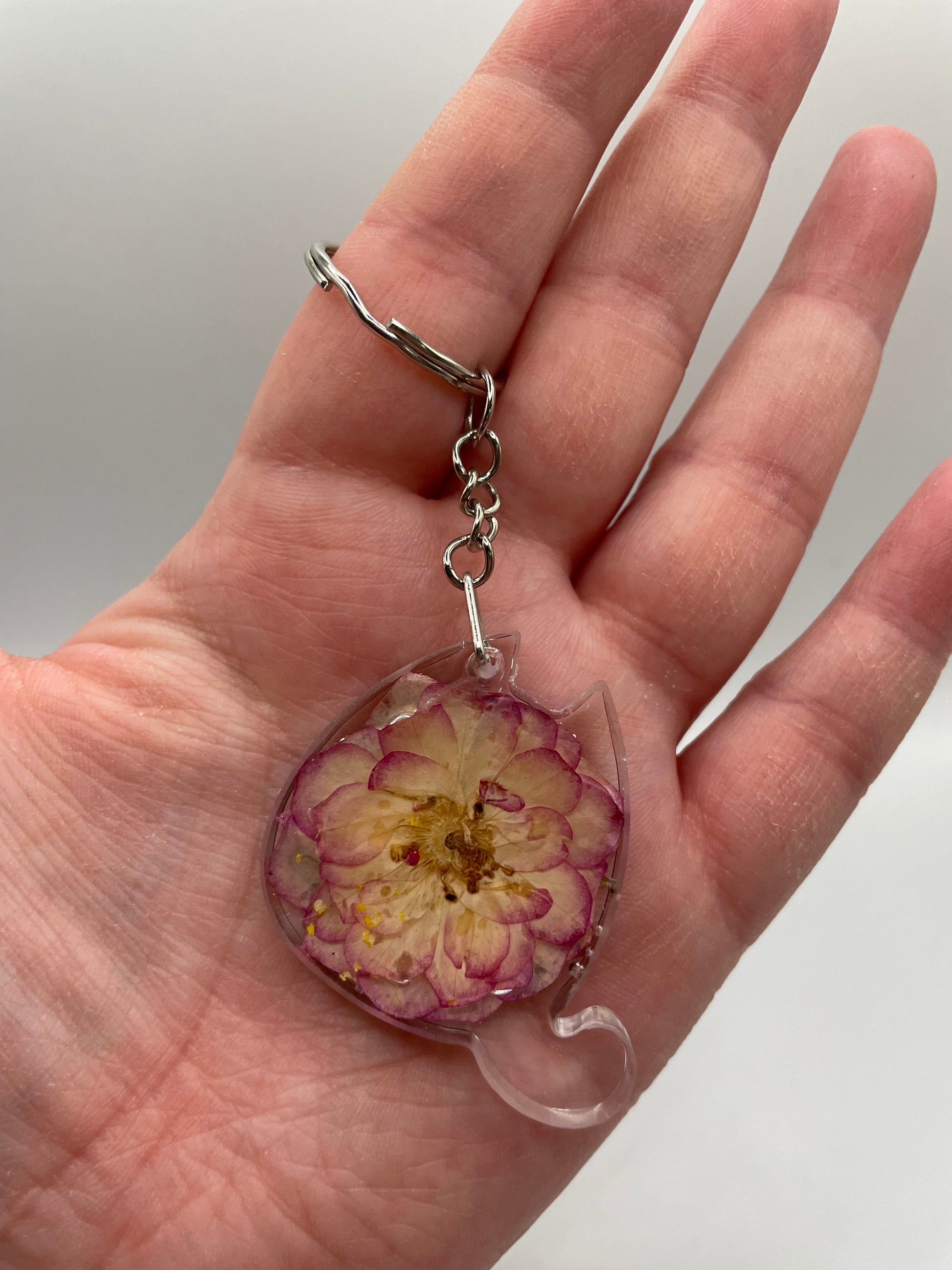 Hand holding a keychain with a pressed flower design against a plain background