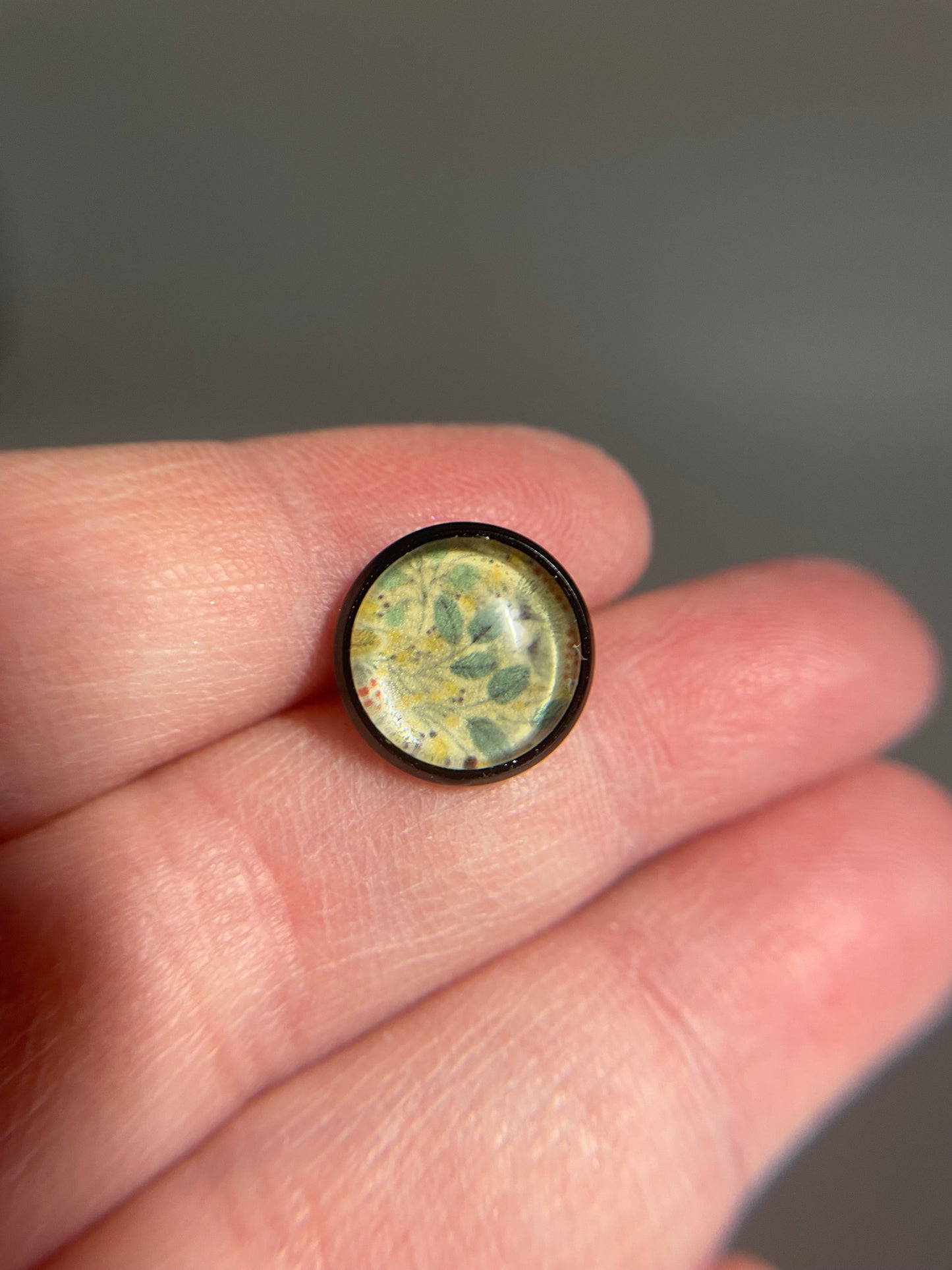 Round, transparent object with green and yellow pattern held between fingers against a blurred background