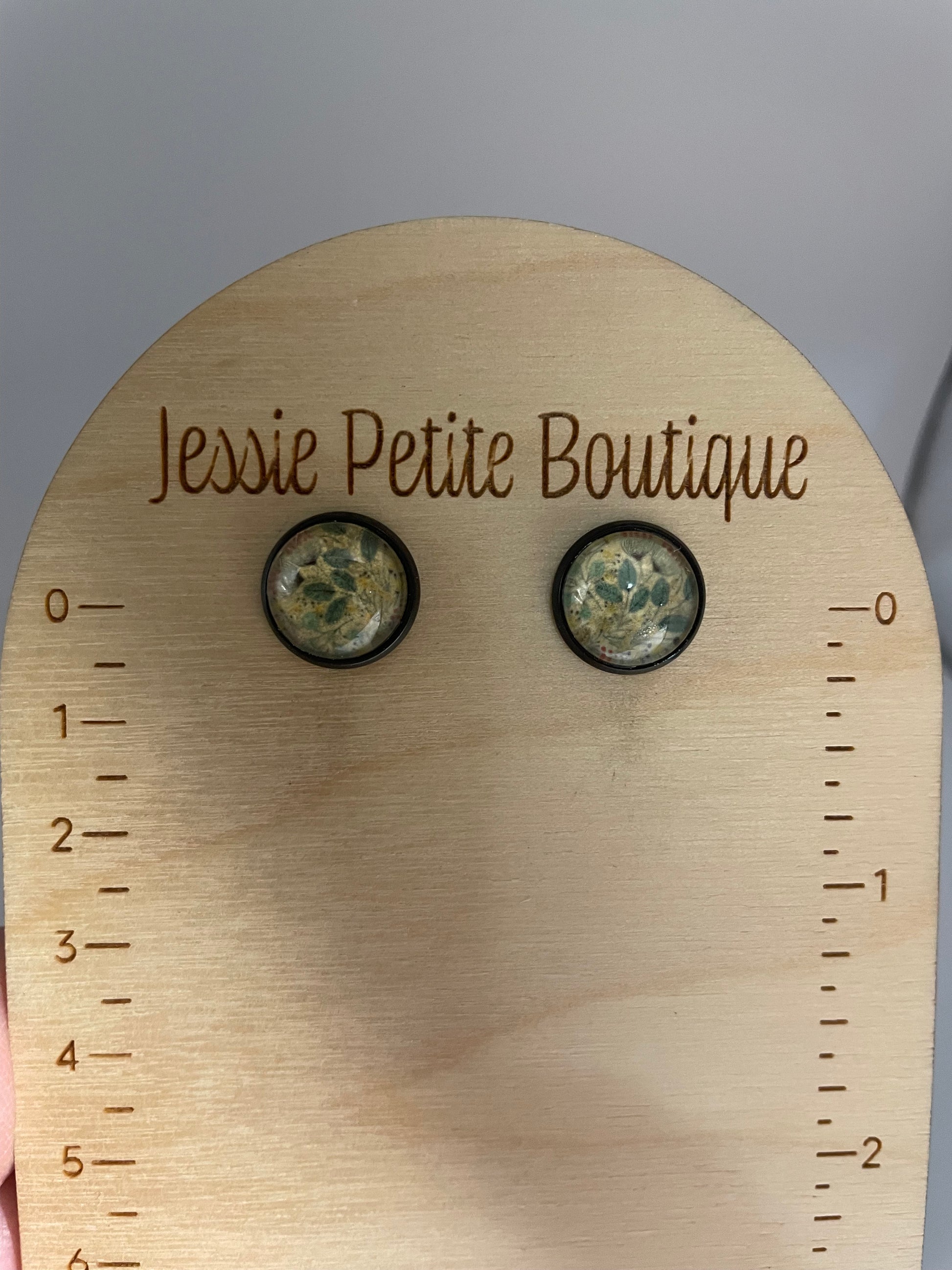Pair of earrings on a wooden display card with measurement scale and 'Jessie Petite Boutique' branding.