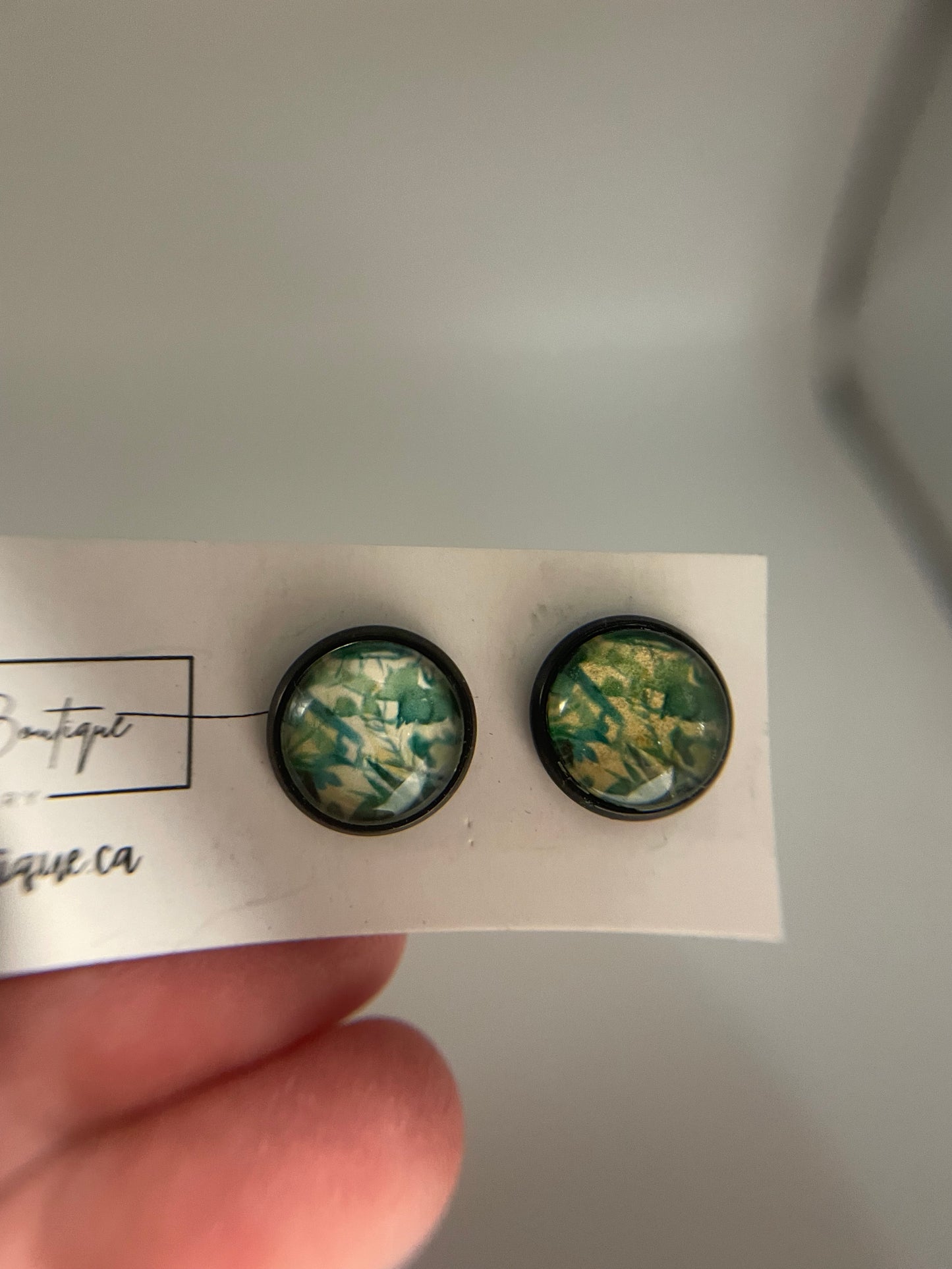 Two green floral earrings on a white card held by a hand against a gray background