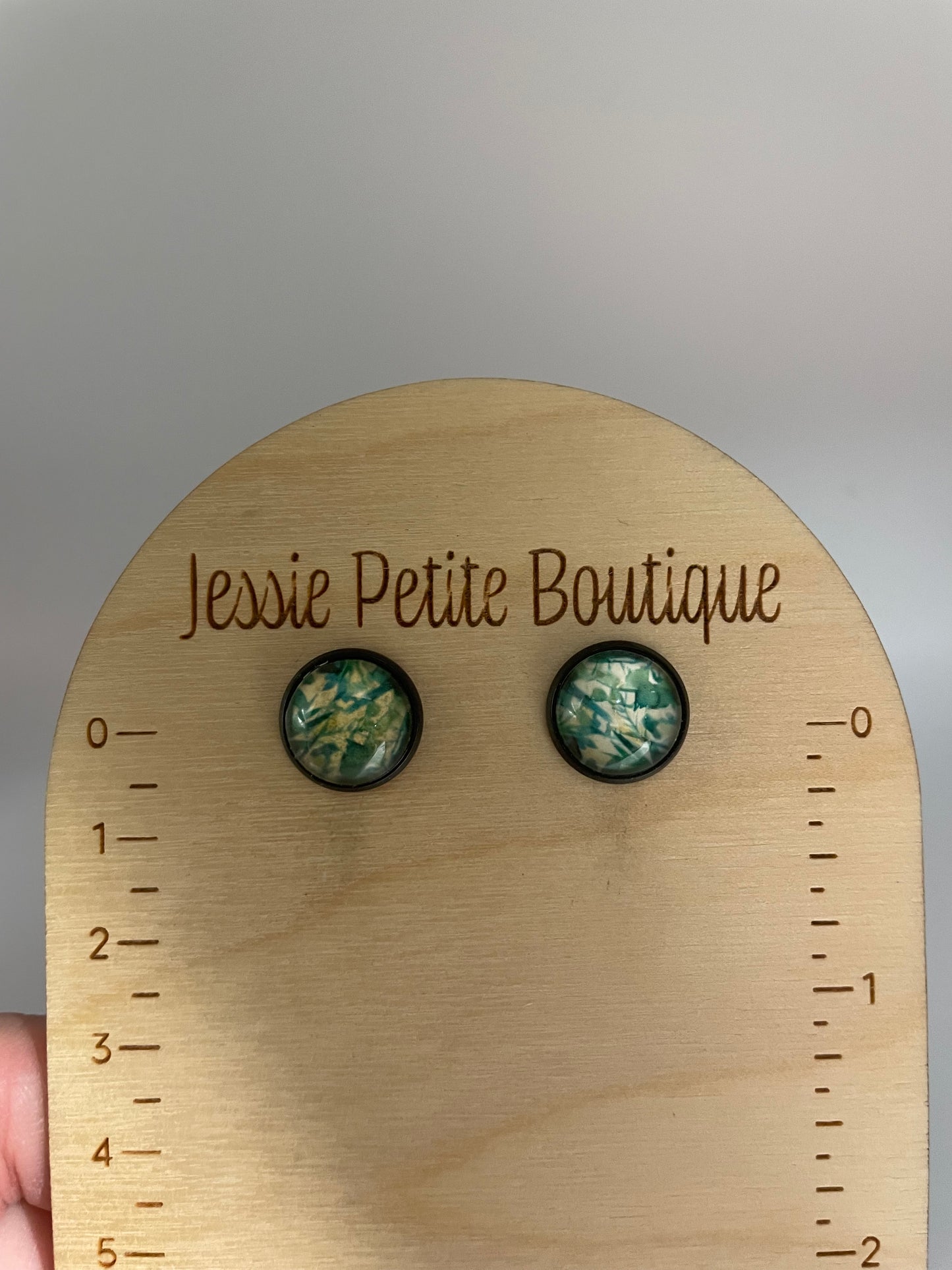 Pair of earrings on a wooden board with measurement scale and 'Jessie Petite Boutique' branding.
