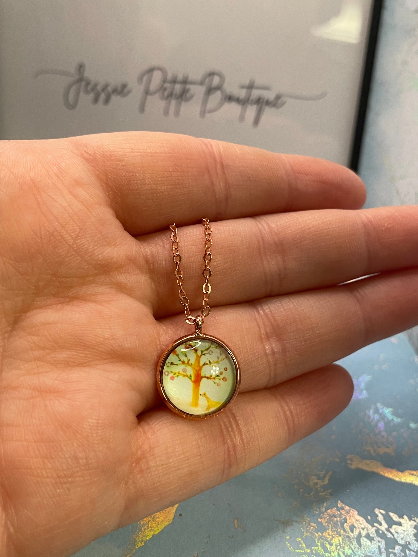 Hand holding a delicate gold necklace with a round pendant against a blurred background
