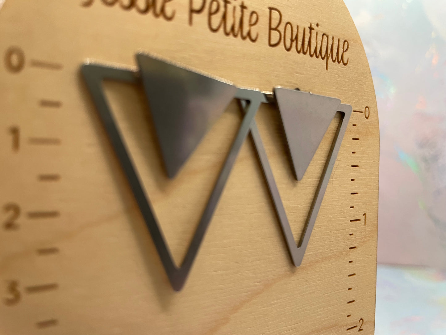 Metal triangle earrings on a wooden scale with 'Petite Petite Boutique' branding.