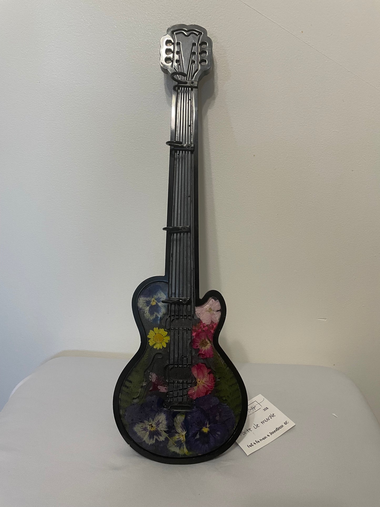Decorative guitar-shaped object with floral design on a white surface