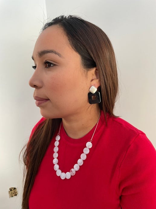 Woman wearing a red top and white beaded necklace with earrings, against a plain background.