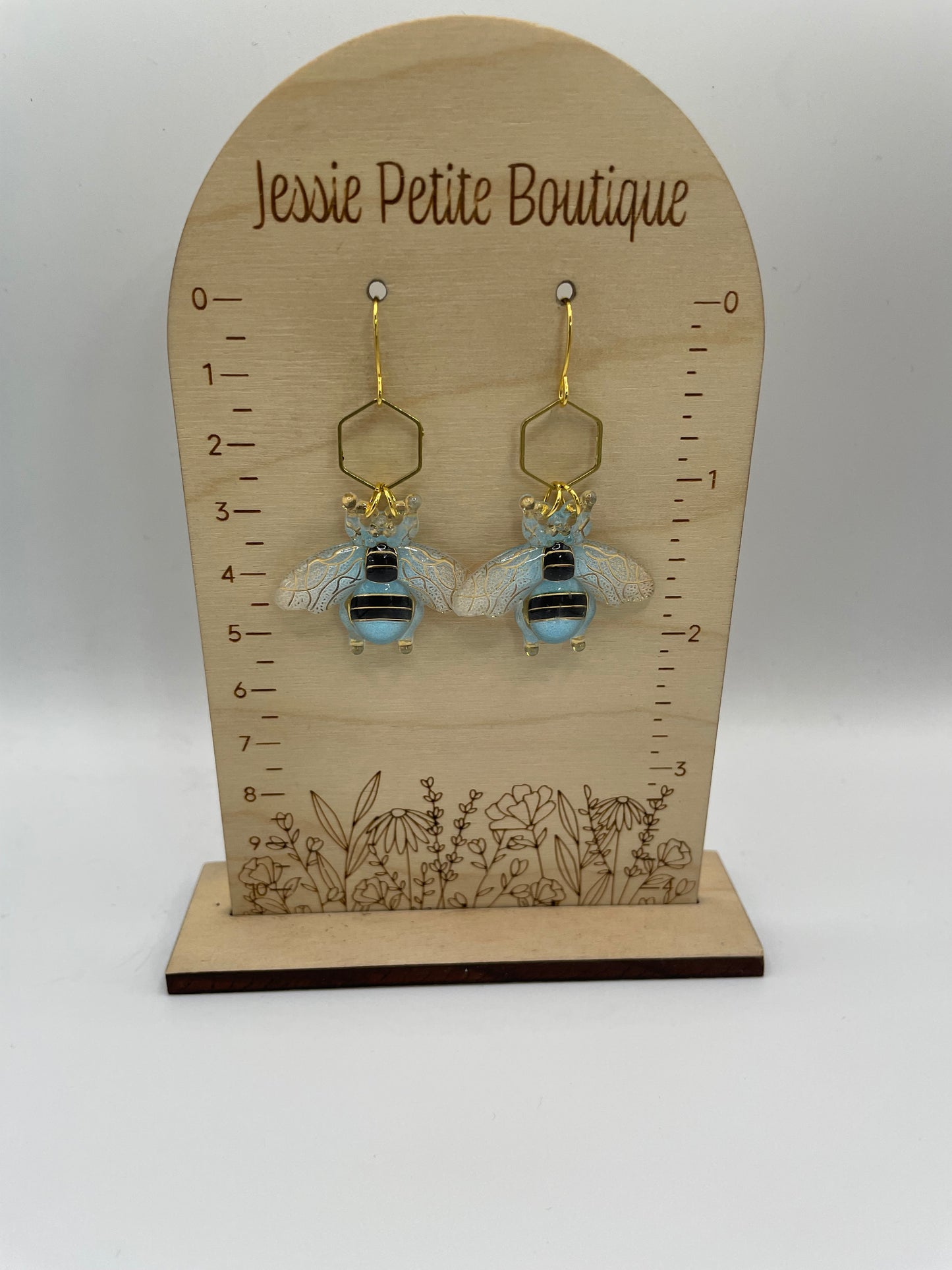 Pair of bee-shaped earrings on a wooden display card with measurements, branded 'Jessie Petite Boutique'.