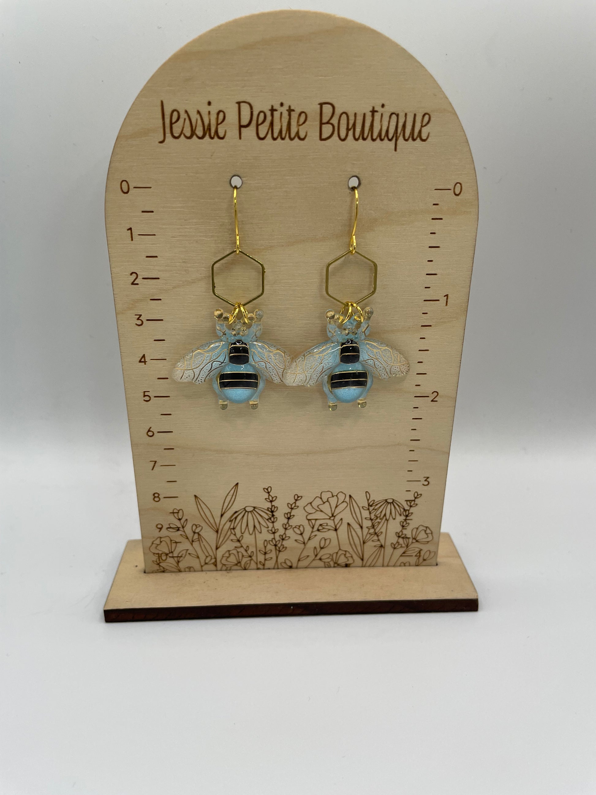Pair of bee-shaped earrings on a wooden display card with measurements, branded 'Jessie Petite Boutique'.