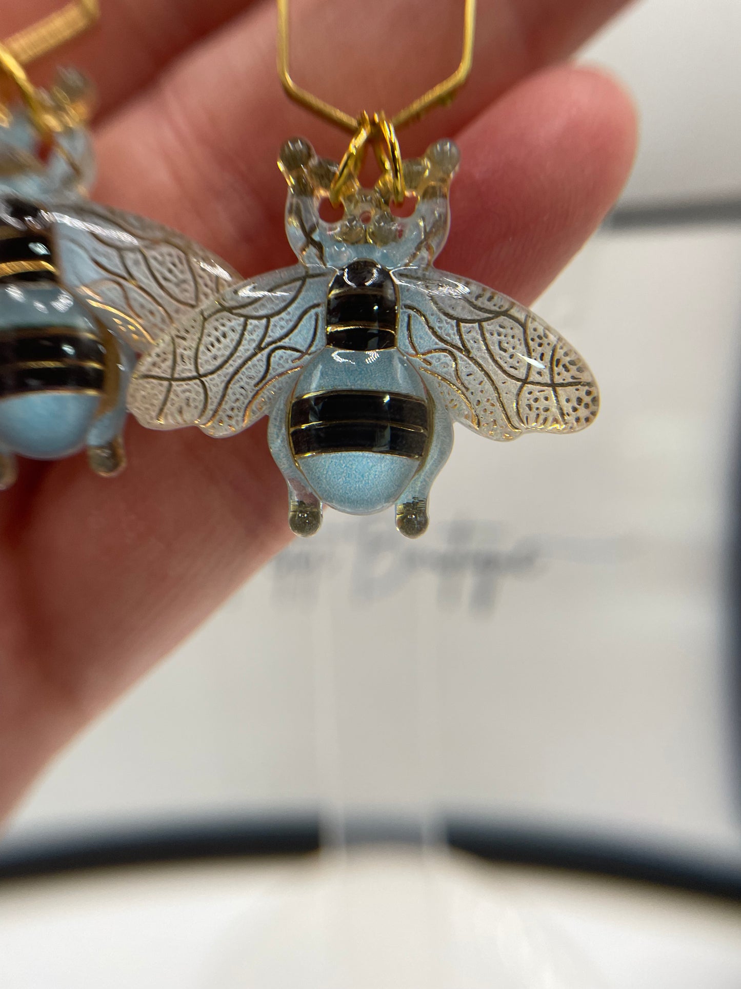 Decorative bee earrings held by a hand with a blurred background
