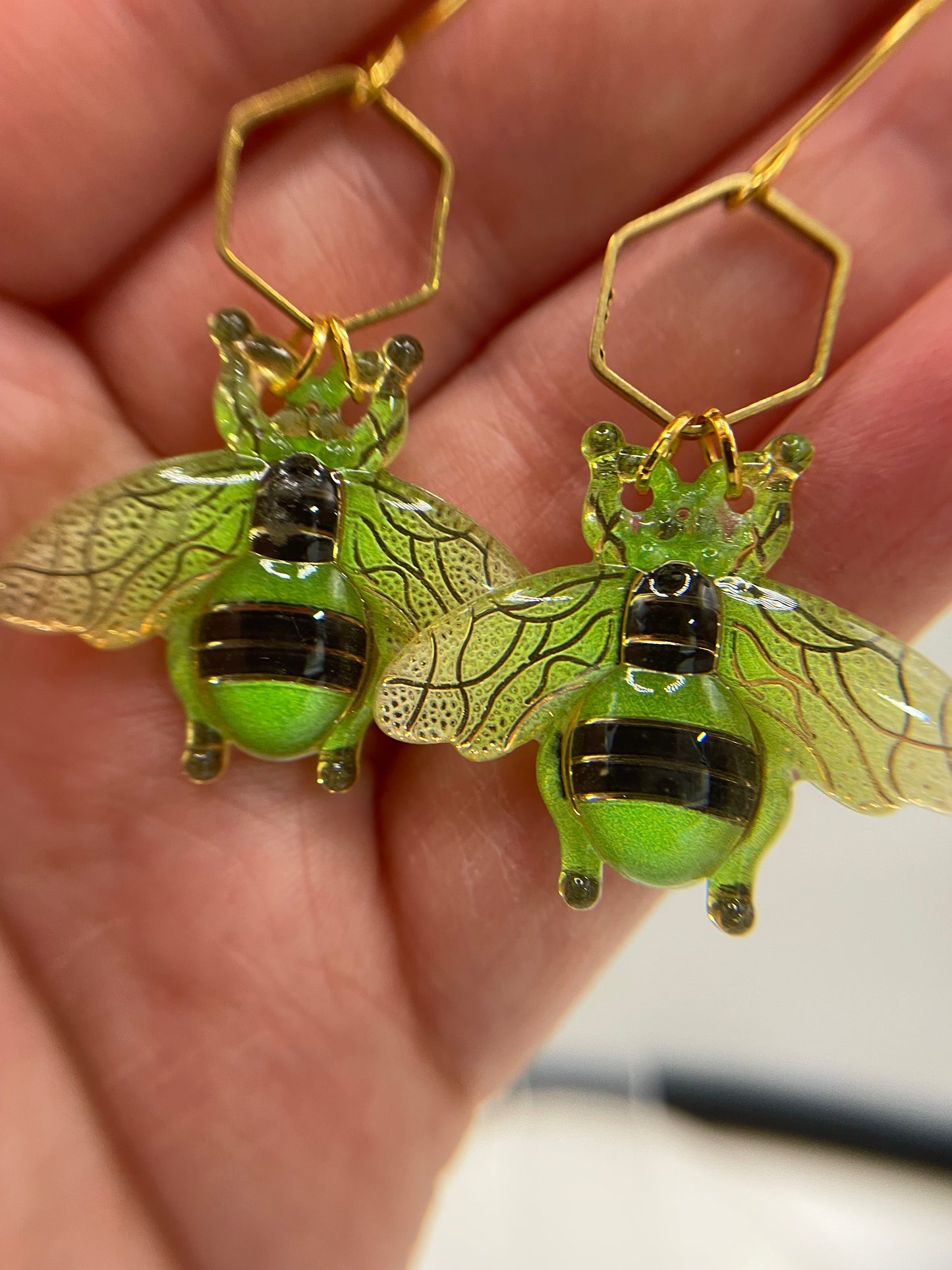 Green bee-shaped earrings held in a hand with a blurred background