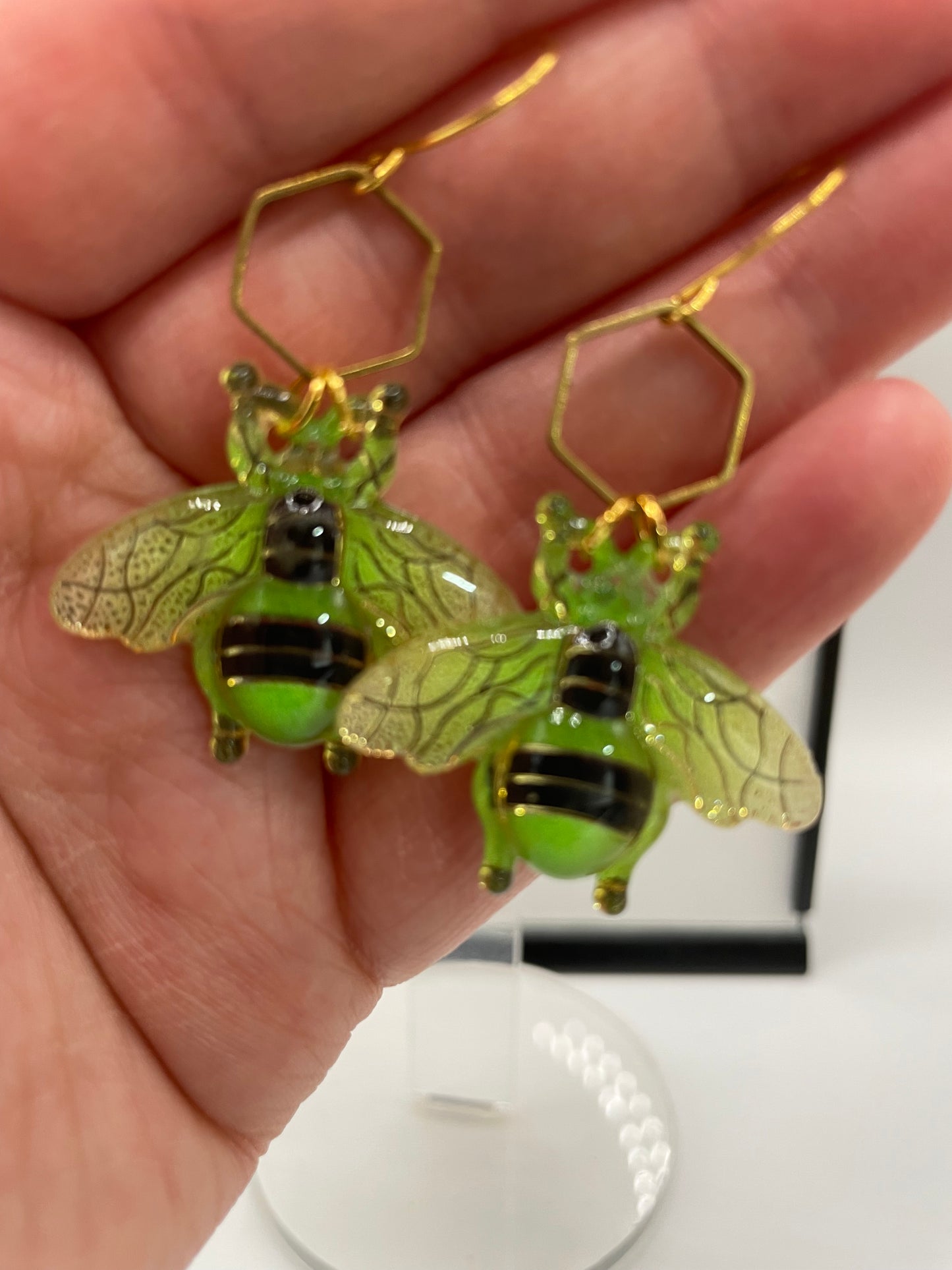 Green bee-shaped earrings held in a hand with a blurred background