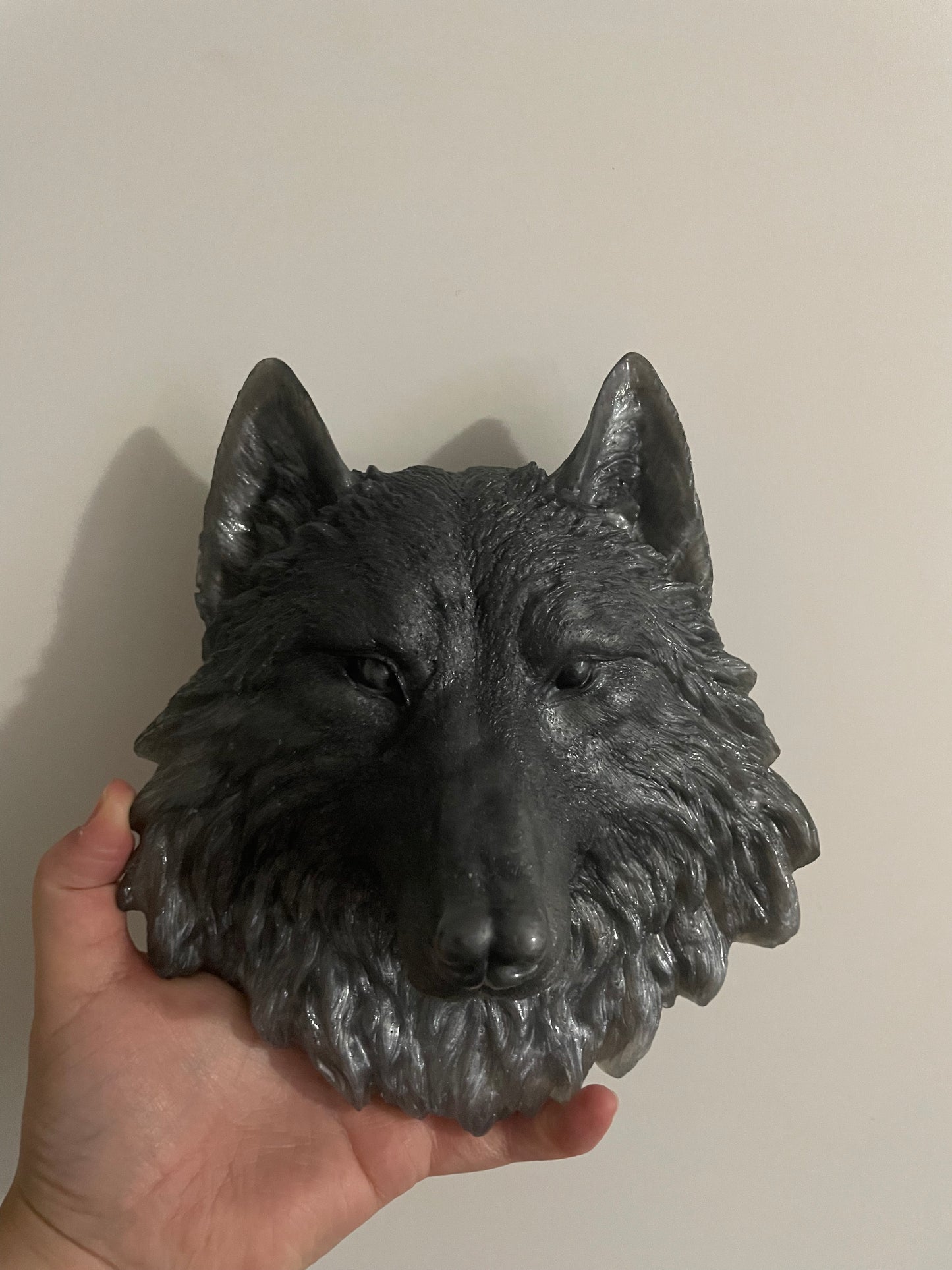 Hand holding a black wolf head sculpture against a plain background