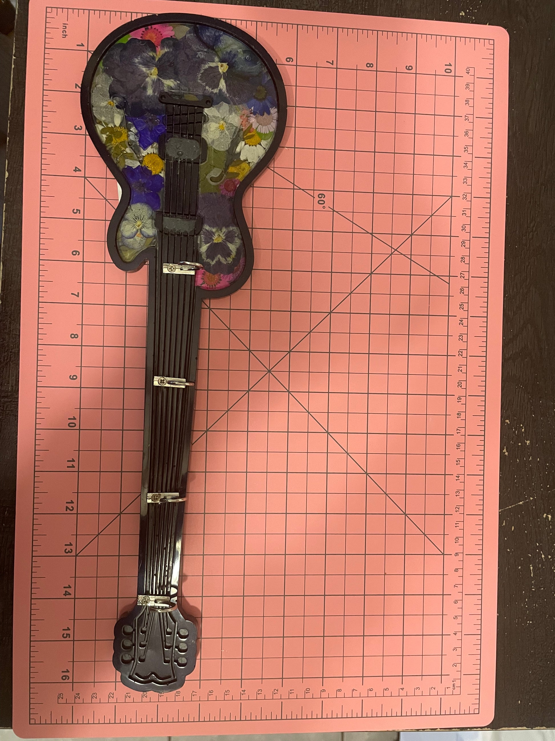 Decorative guitar-shaped object on a pink cutting mat with grid lines