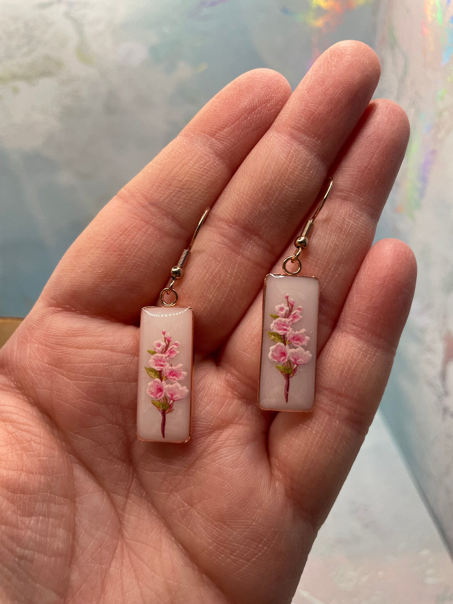 Hand holding two small rectangular charms with floral designs against a blurred background