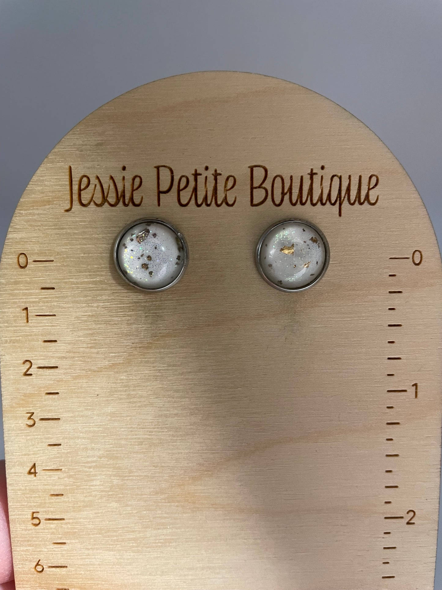Pair of earrings on a wooden measurement tool with 'Jessie Petite Boutique' branding.