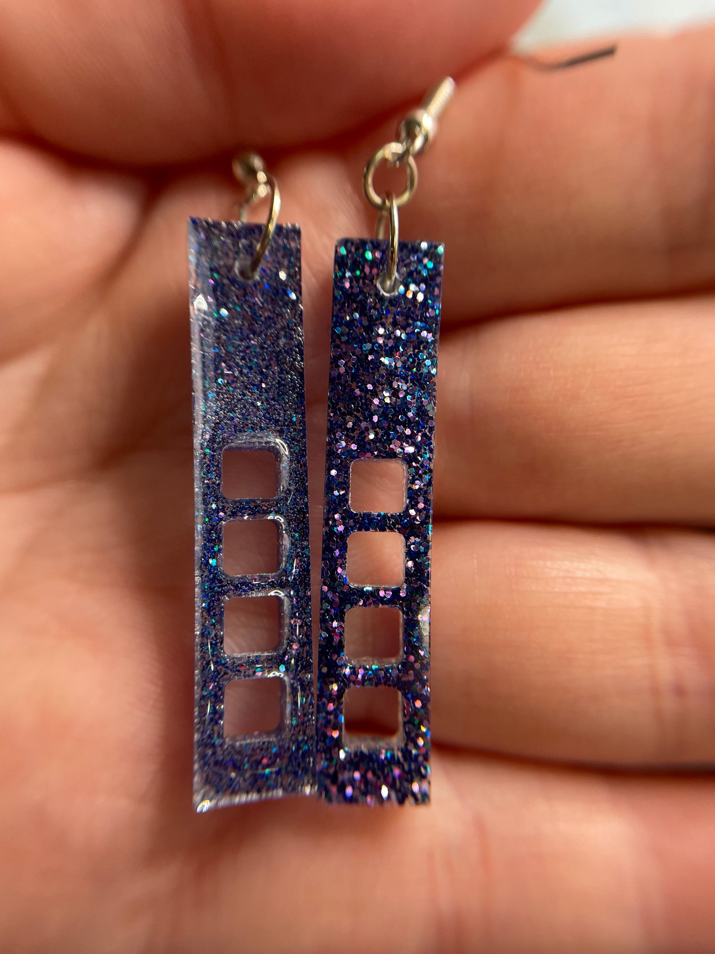 Pair of sparkly purple:skyscraper earrings held between fingers showing the front and the back