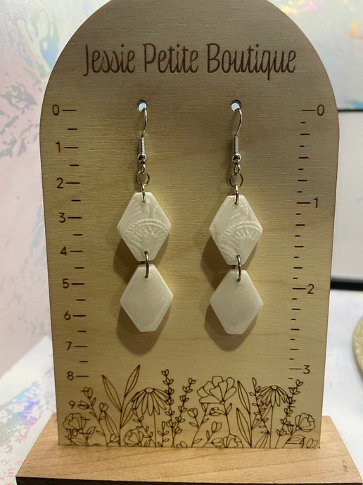 Pair of white geometric earrings on a wooden display card with 'Jessie Petite Boutique' branding.
