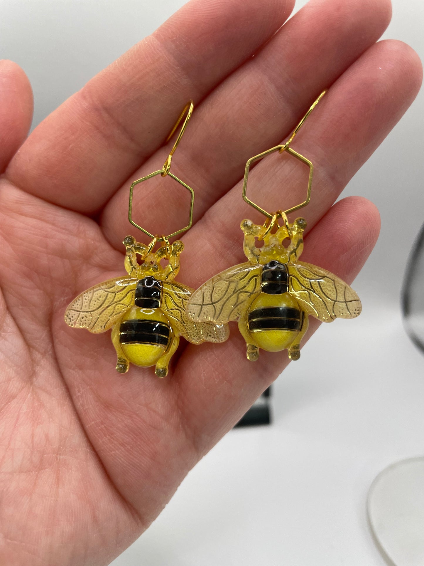 Gold bee-shaped earrings held in a hand against a white background