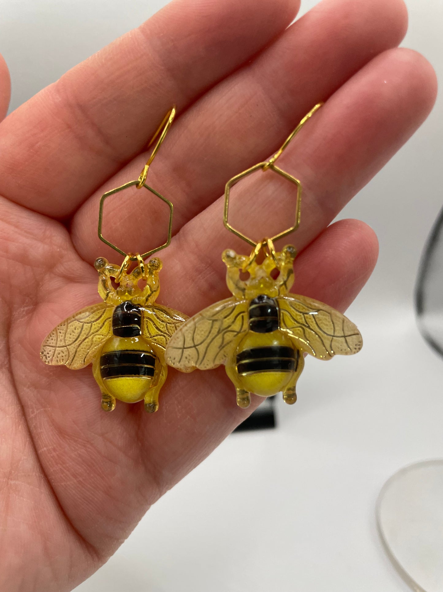 Gold bee-shaped earrings held in a hand against a neutral background