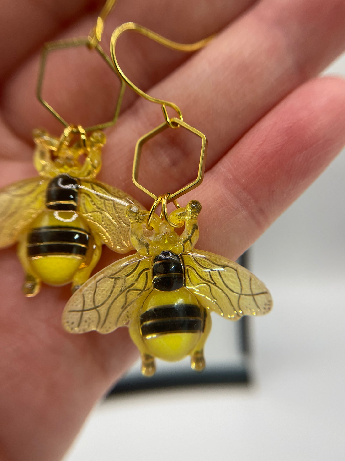 Gold bee-shaped earrings held in a hand with a blurred background