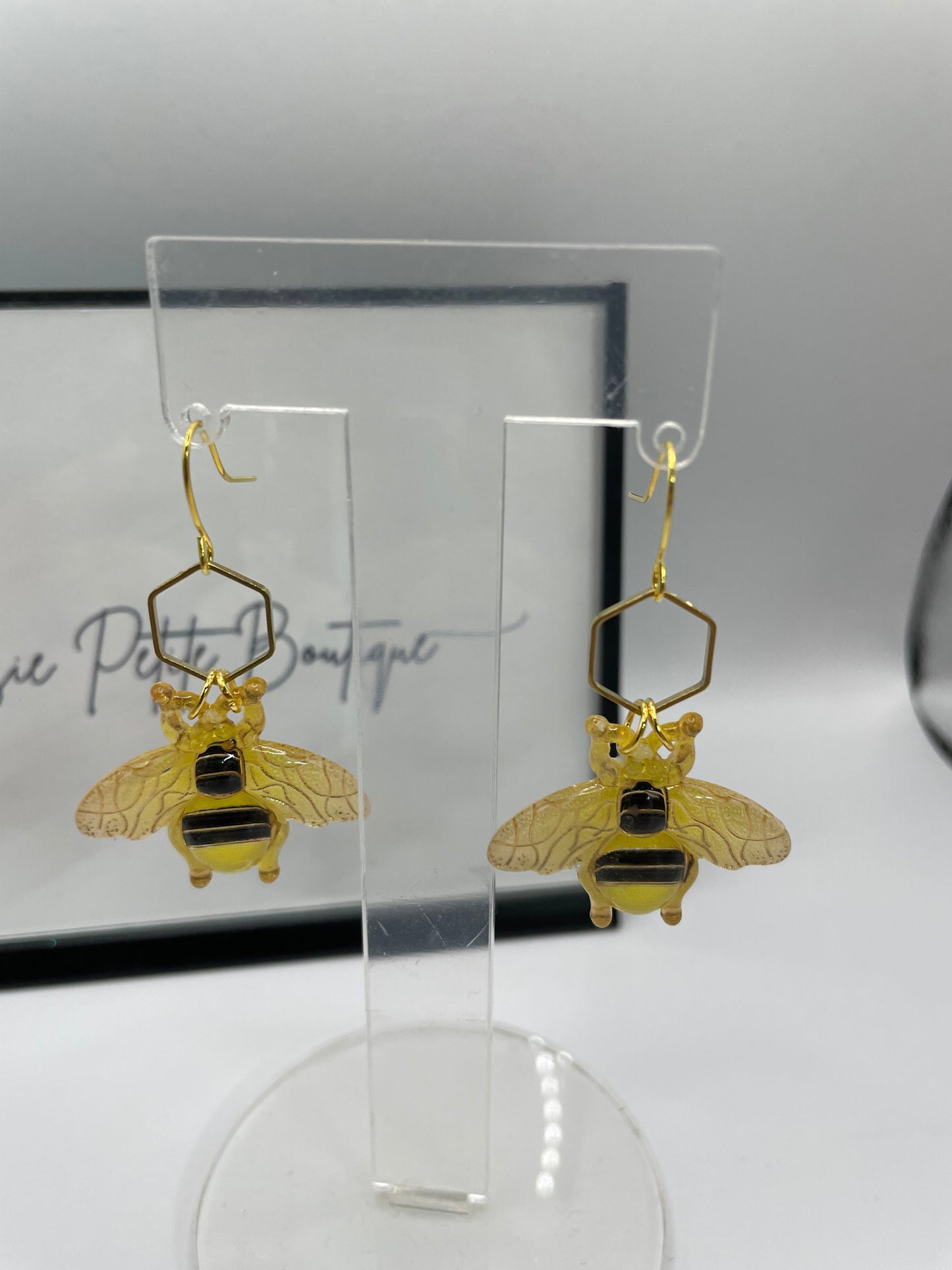 Gold bee-shaped earrings on a clear stand with a blurred background