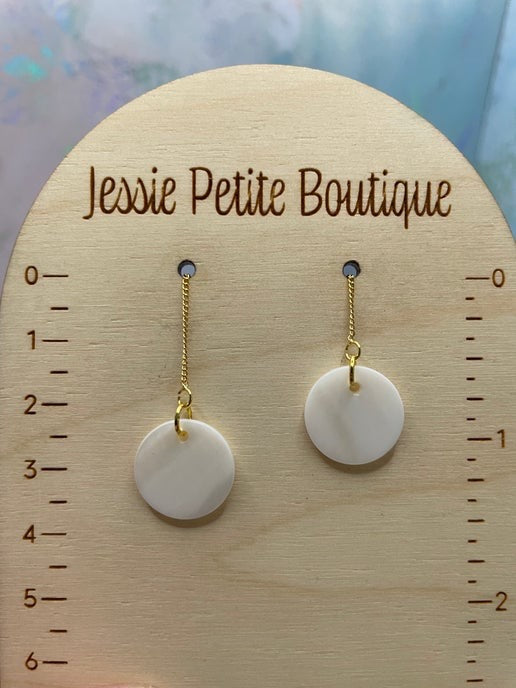 Pair of white circular earrings on a wooden display card with measurement scale, branded 'Jessie Petite Boutique'.