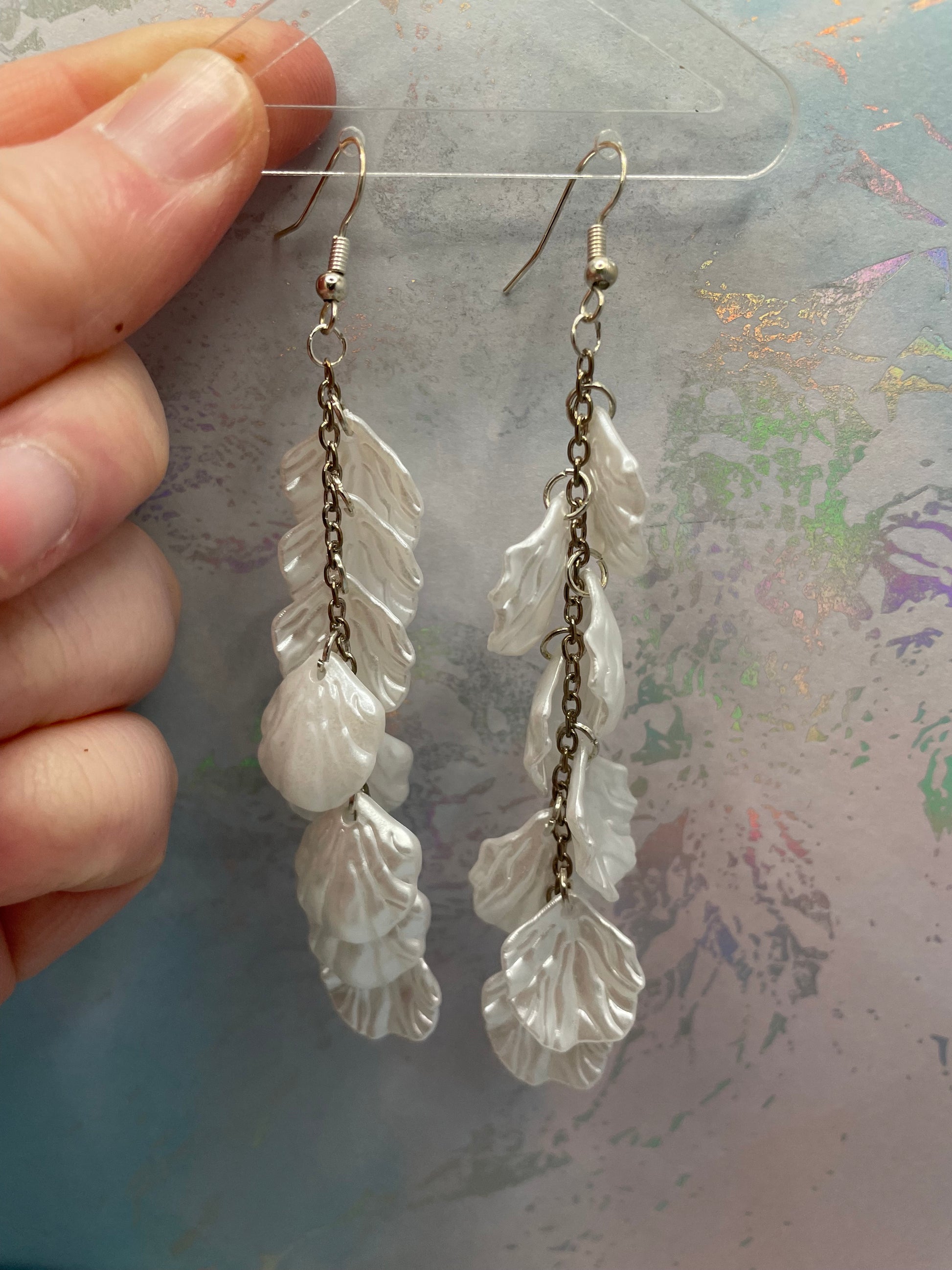 10.3cm-White Flower Petal Acrylic Dangle Earrings with a chain held by a hand against a textured background