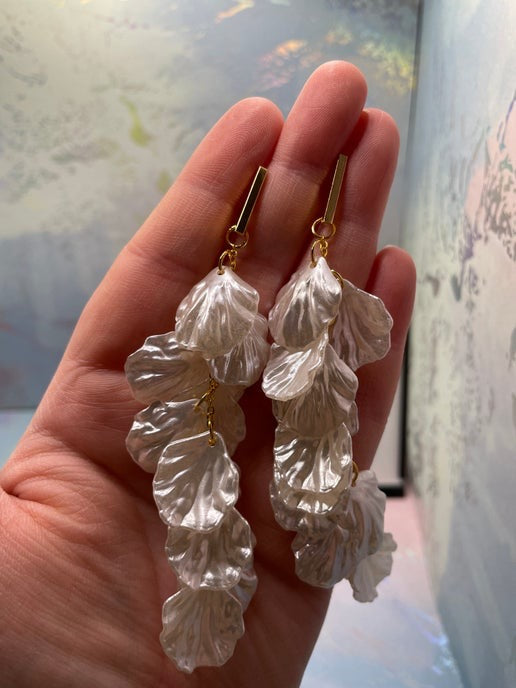 White leaf-shaped earrings on gold hooks held in a hand with a blurred background