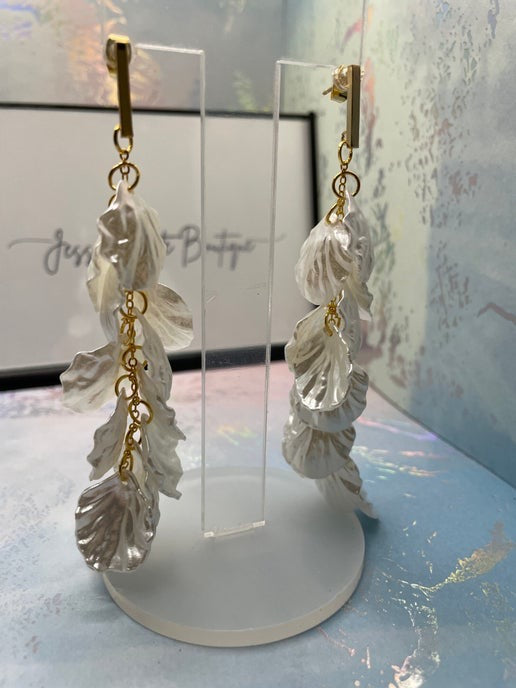 Pair of shell-shaped earrings with gold accents on a stand.
