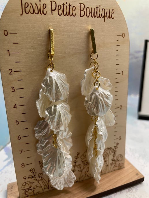 Pair of leaf-shaped earrings on a wooden stand with 'Jessie Petite Boutique' branding.