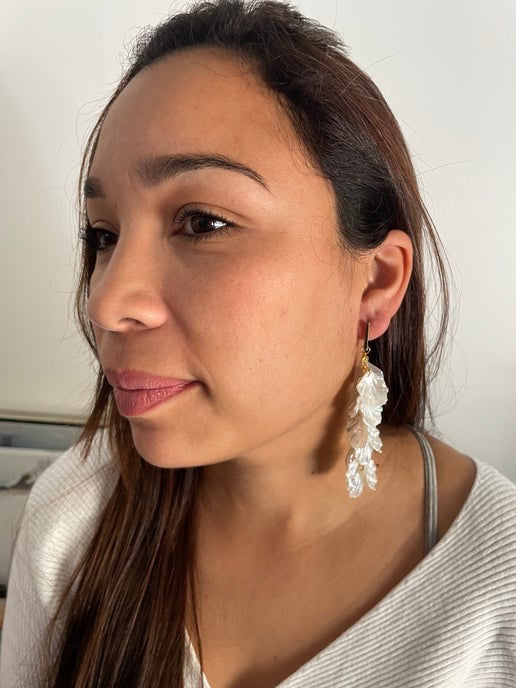 Woman wearing white floral earrings against a neutral background