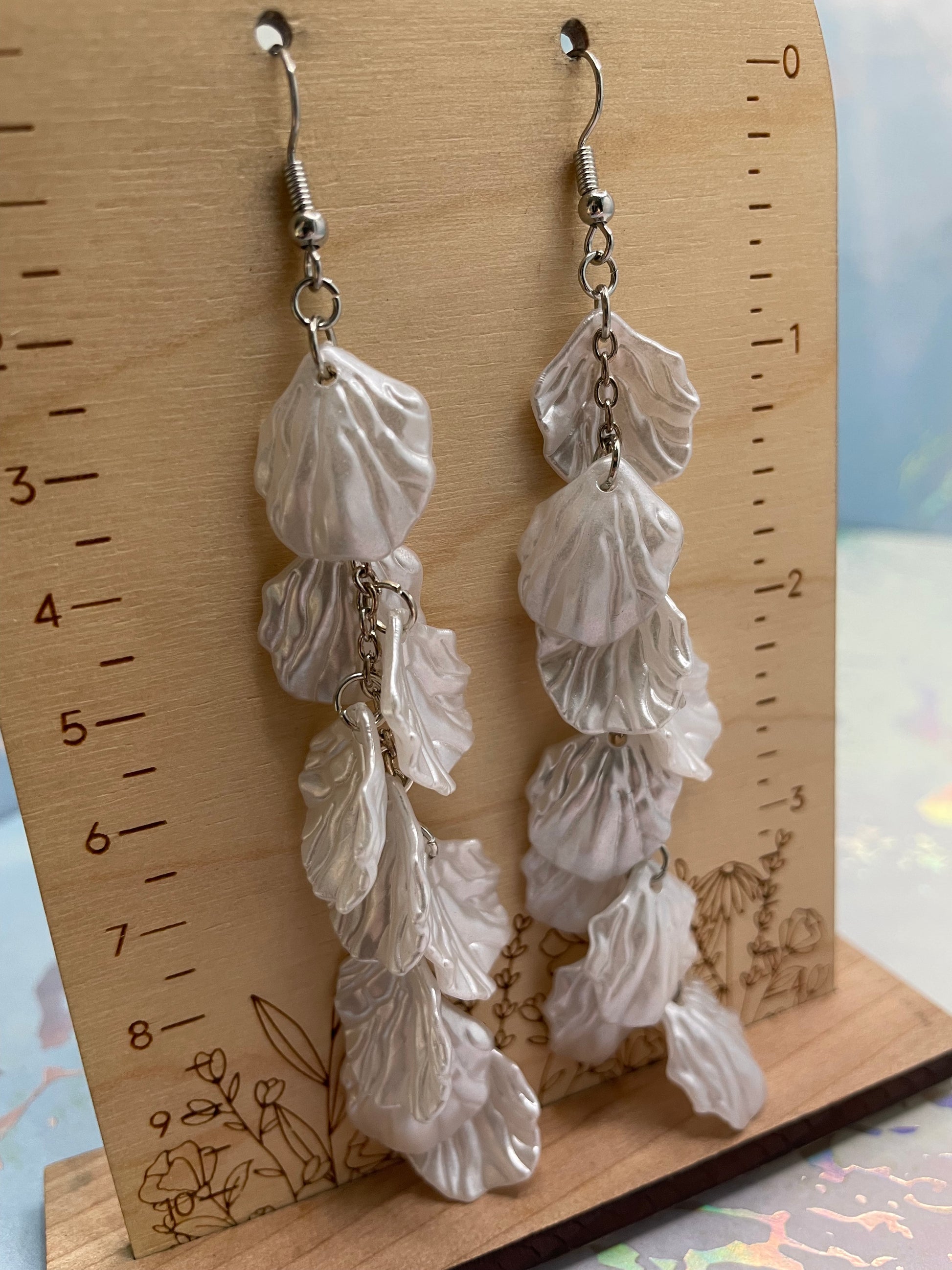 White leaf-shaped earrings on a wooden surface with a ruler for scale.