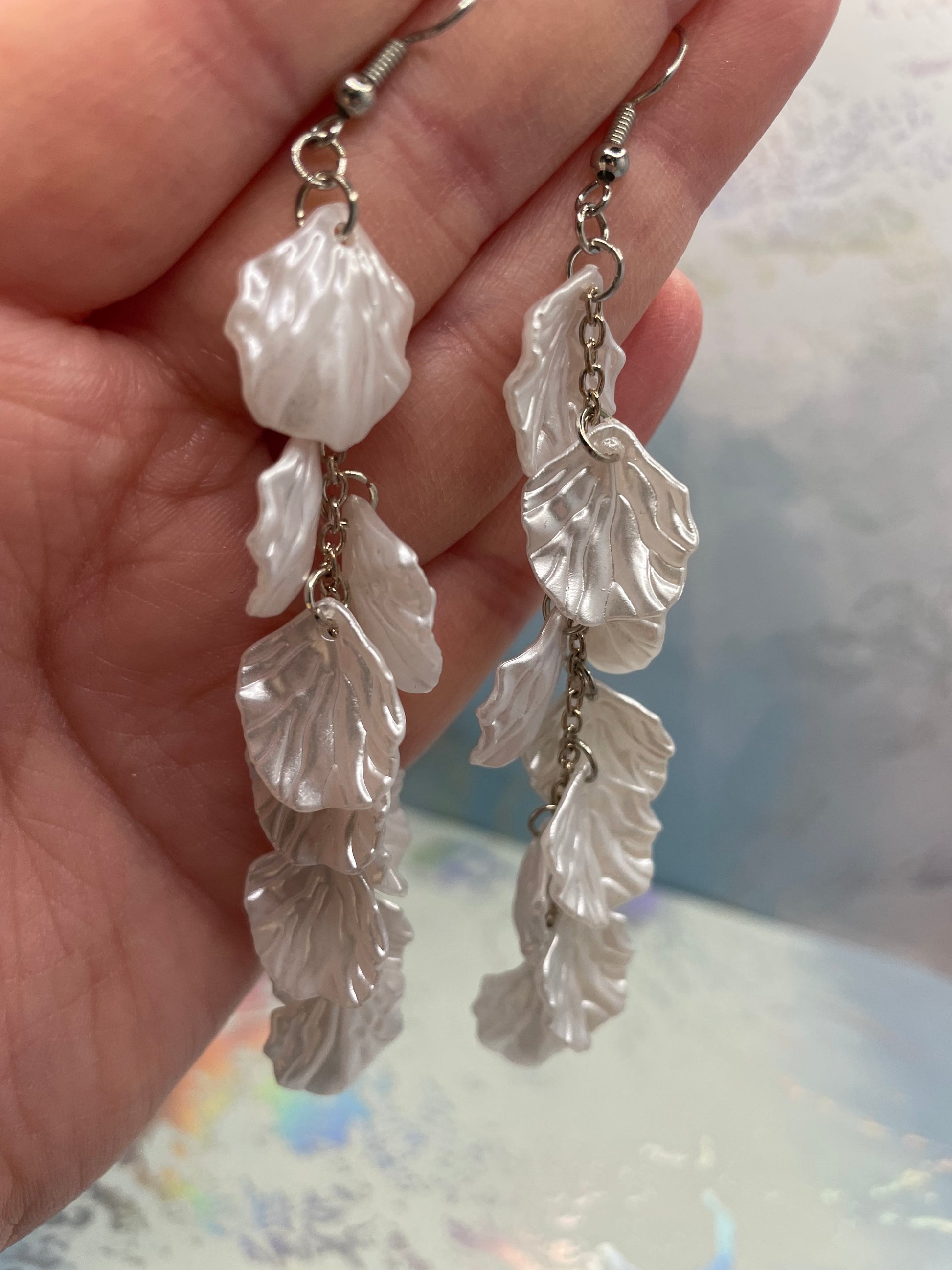 11cm-White Flower Petal Acrylic Dangle Earrings held in a hand with a blurred background