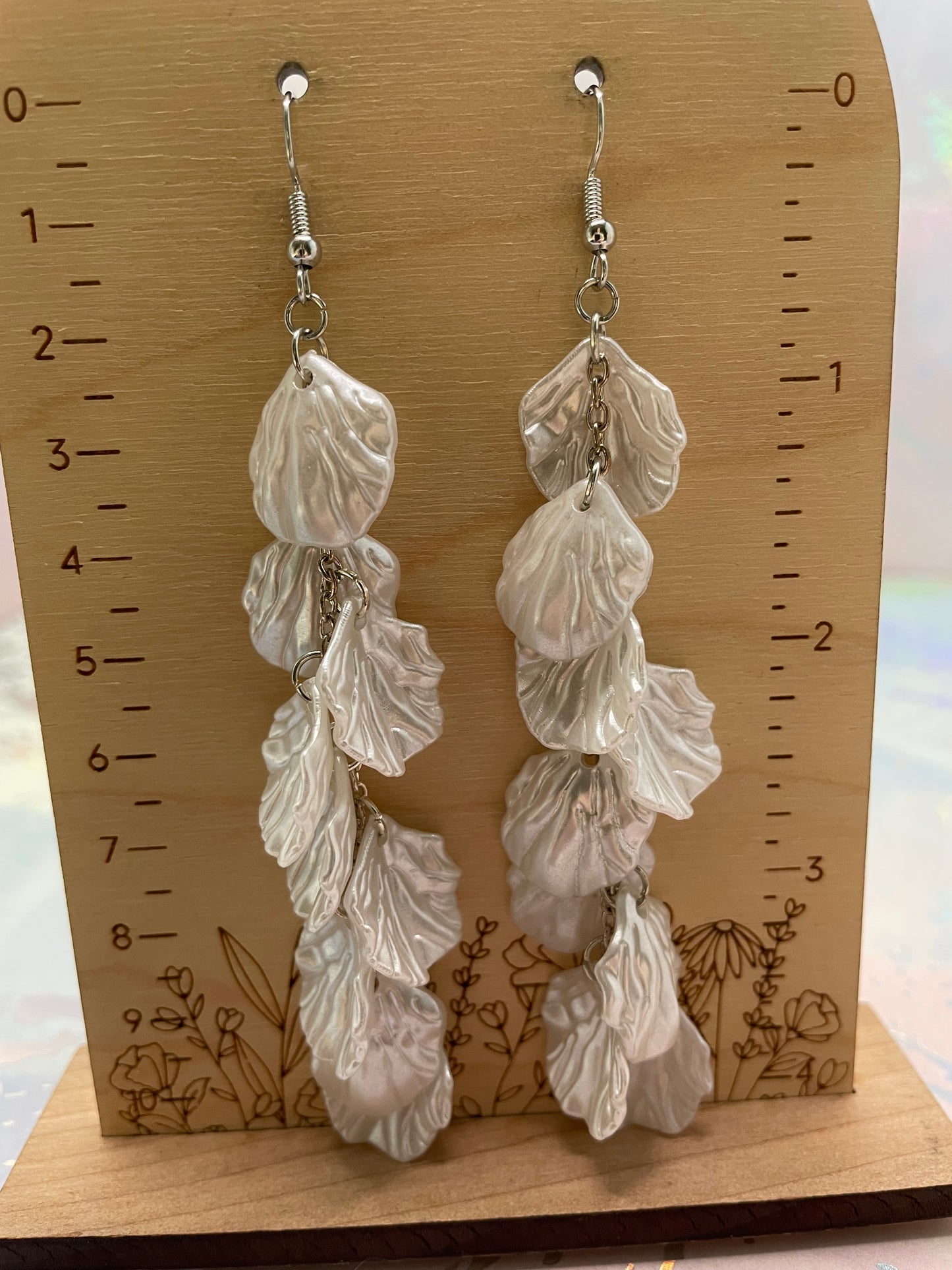 Silver leaf-shaped earrings on a wooden board with measurement scale