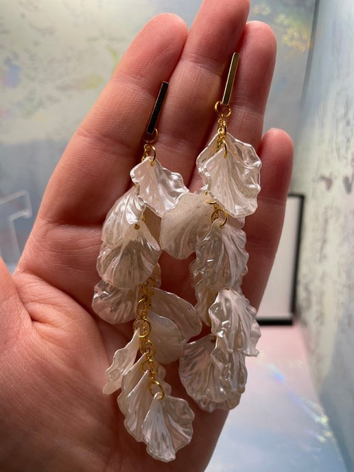 Hand holding a pair of leaf-shaped earrings with gold accents.