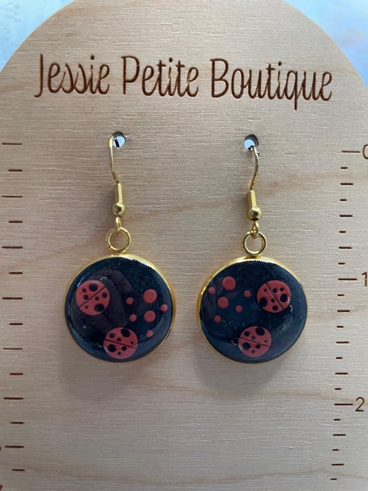 Black earrings with red polka dots+ladybugs on a wooden card from Jessie Petite Boutique.