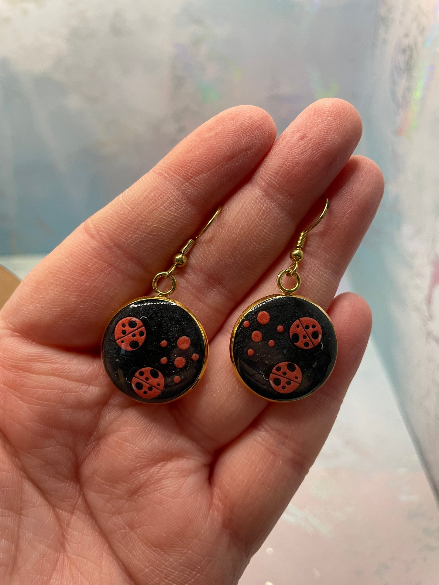 Black earrings with gold accents held in a hand against a light background