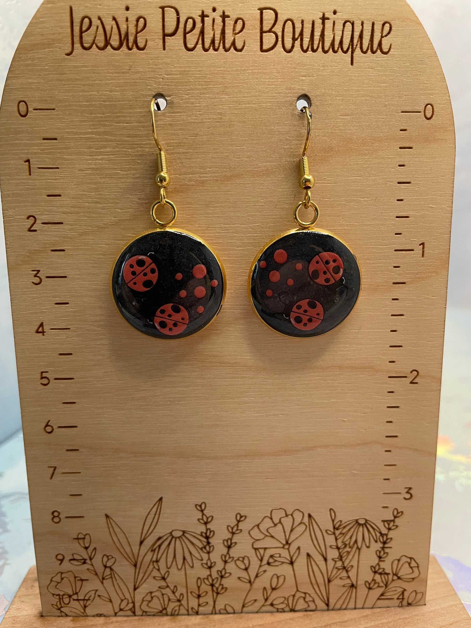 Pair of earrings on a wooden card with floral design and measurement scale.