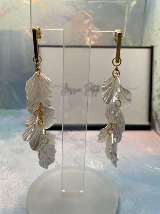 Leaf-shaped earrings on a clear stand with a blurred background