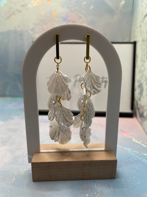 White leaf-shaped earrings on a wooden stand with a white arch background