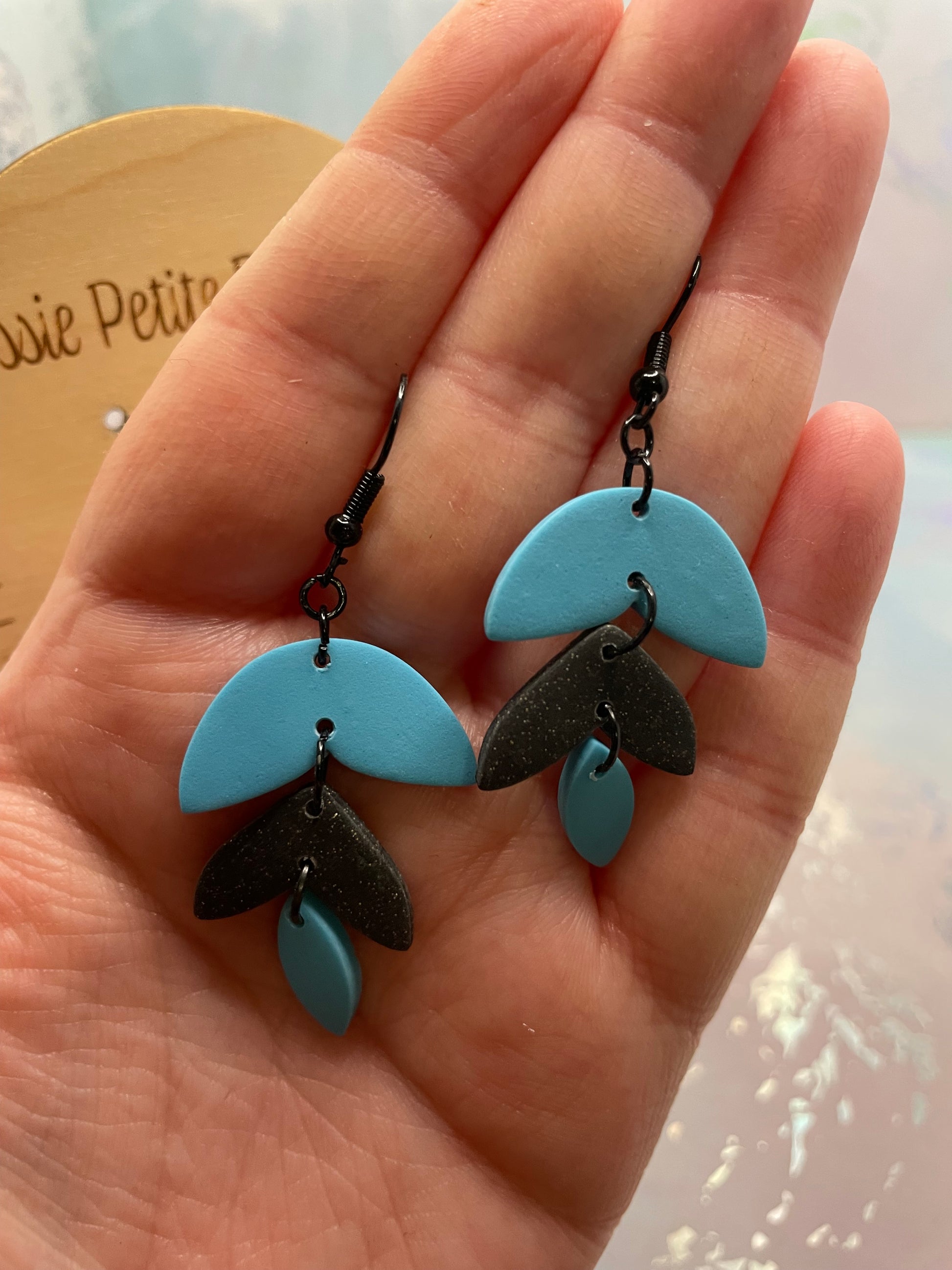 Blue and black Alba earrings held in a hand with a blurred background