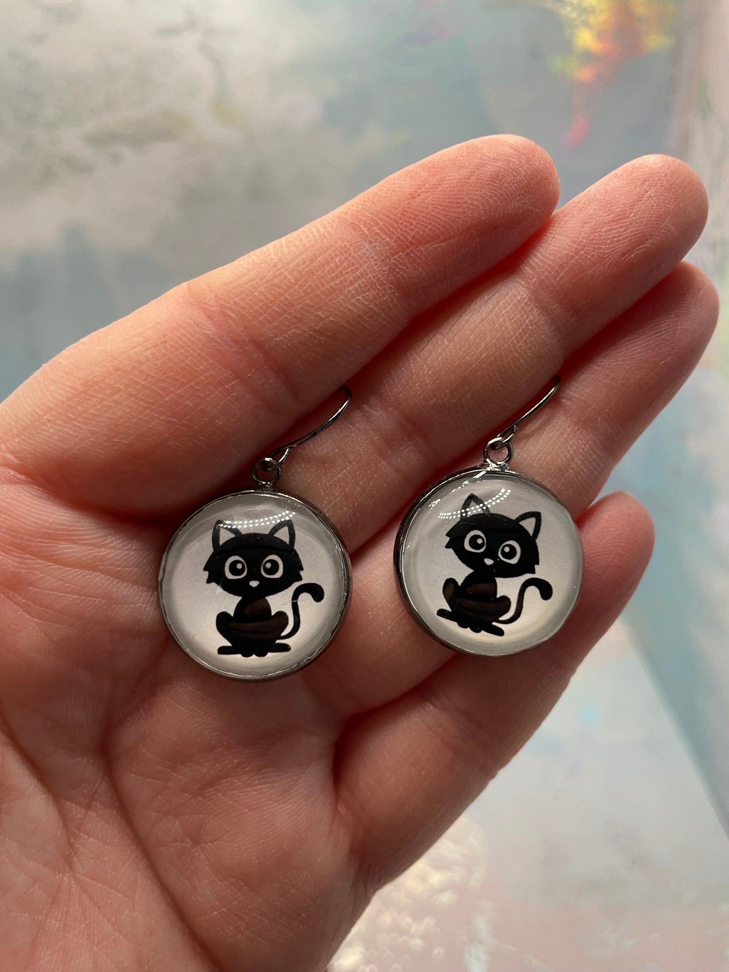 Two round gun metal bezel with black cat illustrations held in a hand against a blurred background.