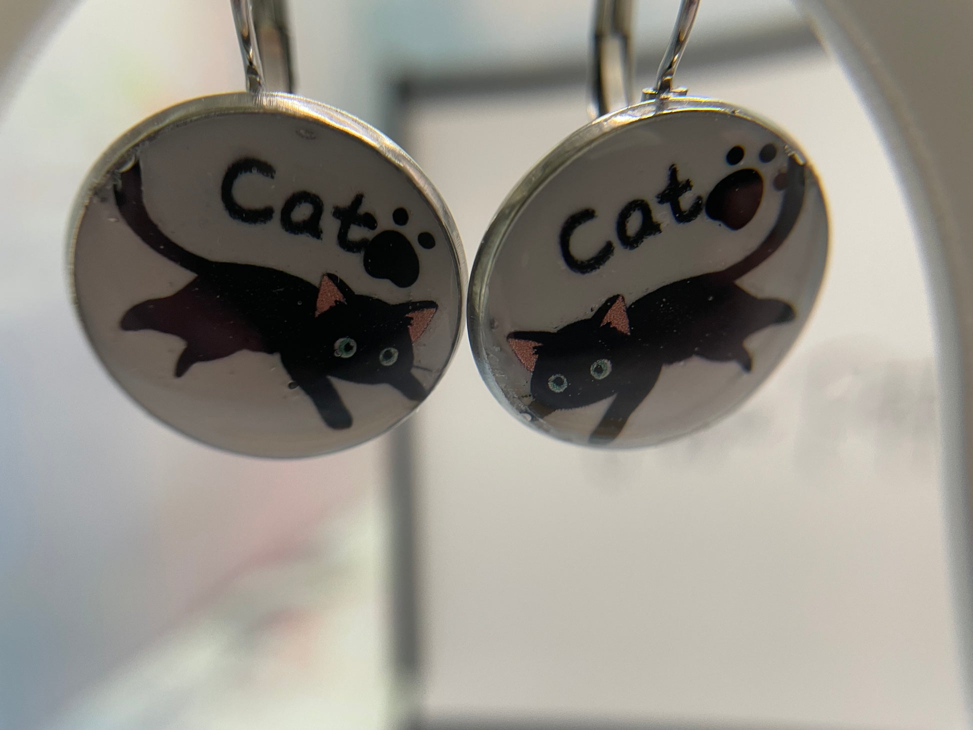 Pair of earrings with black cat illustrations and 'Cat' text on silver backgrounds.
