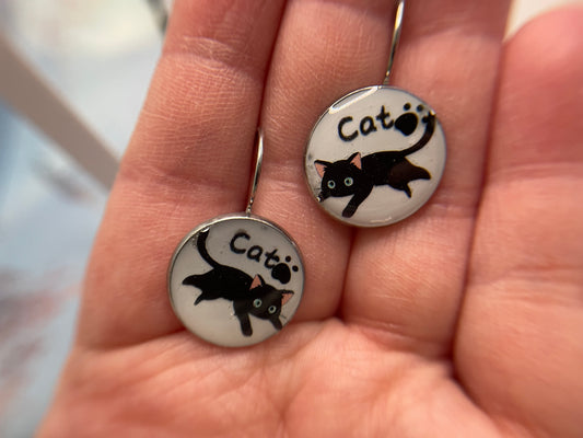 Pair of earrings with cat illustrations held between fingers