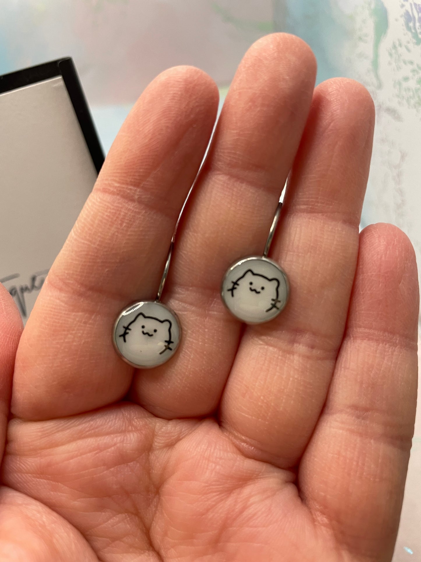 Two small round earrings with a face design held between fingers.