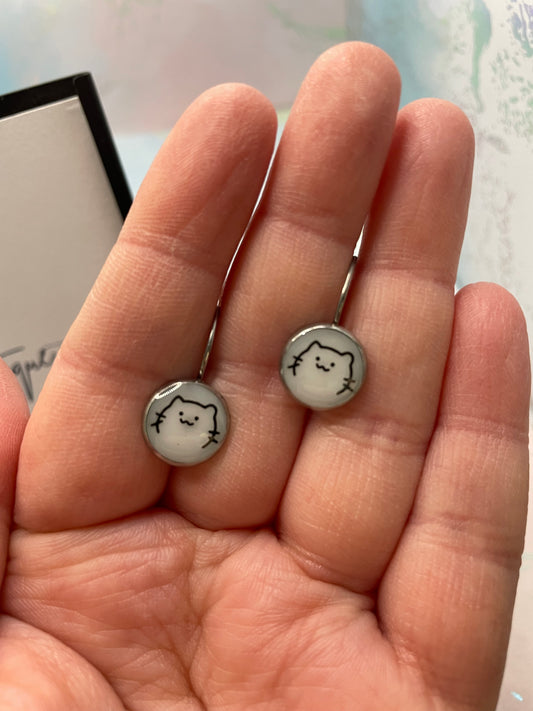 Two small round earrings with a face design held between fingers.