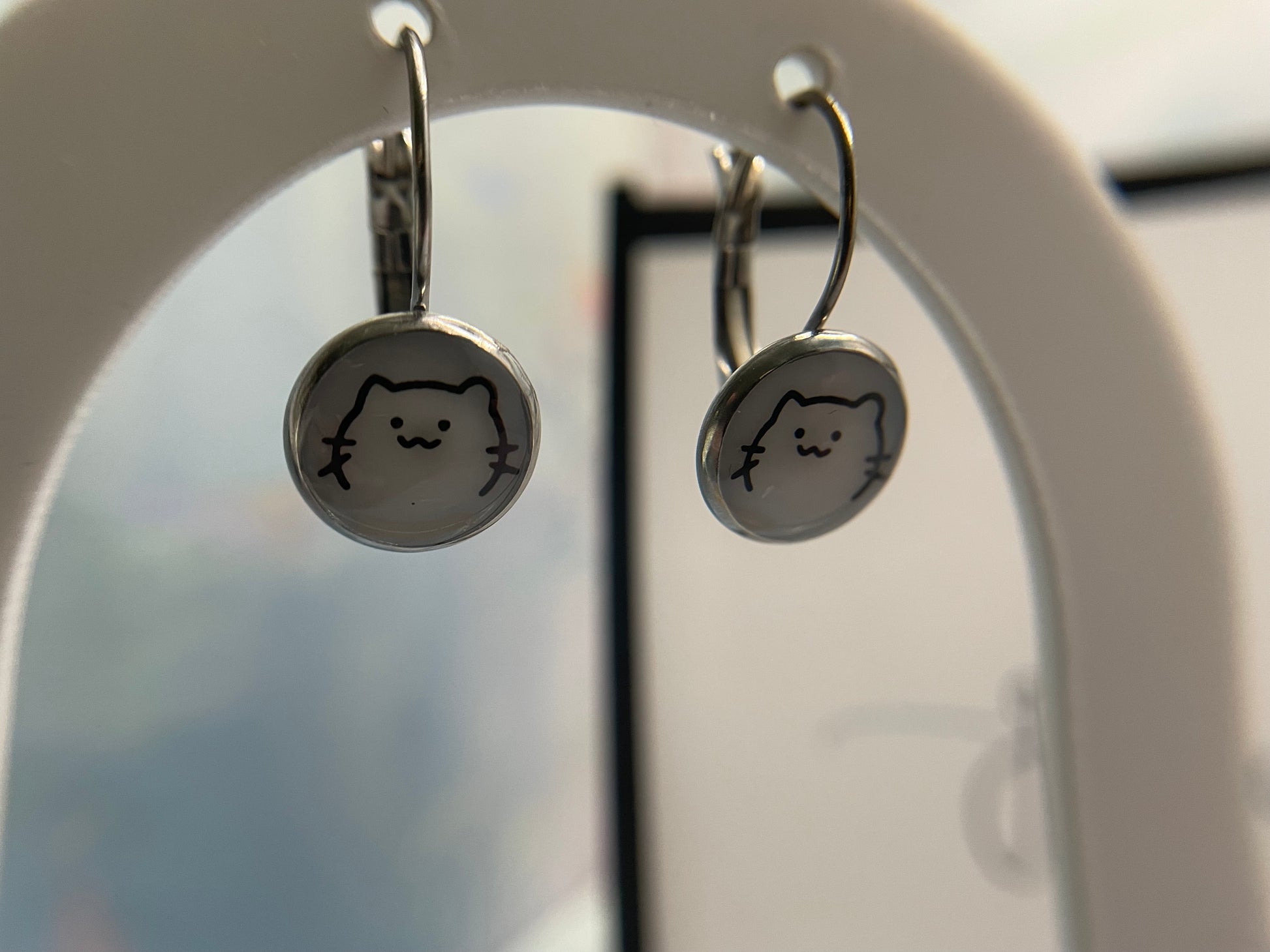 Cat-shaped earrings hanging on a mirror.